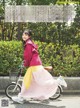 A woman riding a bike down a street next to a fence.