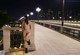 A naked woman standing on a bridge at night.