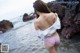 A woman in a white shirt and pink panties standing in the water.