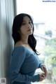 A woman in a blue dress leaning against a window.