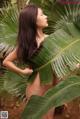 A naked woman standing next to a large green leaf.