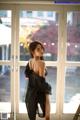 A woman in a black dress standing in front of a window.