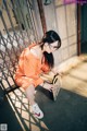 A woman in an orange jumpsuit crouching down with a suitcase.