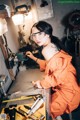 A woman in an orange jumpsuit sitting at a workbench.