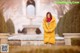 A woman in a yellow coat standing in front of a fountain.