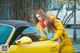 A woman leaning on the door of a yellow car.