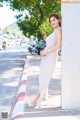 A woman in a white dress leaning against a wall.