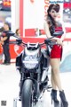 A woman in a red dress standing next to a motorcycle.