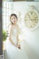 A woman in a wedding dress sitting in front of a clock.