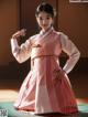 A woman in a pink and white hanbok poses for a picture.