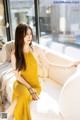 A woman in a yellow dress sitting on a white couch.