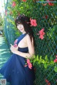 A woman in a blue dress leaning against a fence.