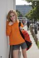 A woman leaning against a wall with a backpack.