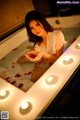 A woman sitting in a bathtub with candles and rose petals.