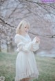 A woman in a white dress standing in front of a tree.