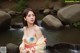 A woman in a yellow kimono standing in front of a waterfall.