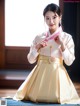 A woman in a yellow and white hanbok is posing for a picture.