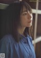 A woman in a blue shirt leaning against a window.